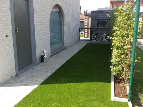 Zijtuin met kunstgras naast een lichte woning, met verharde looppad