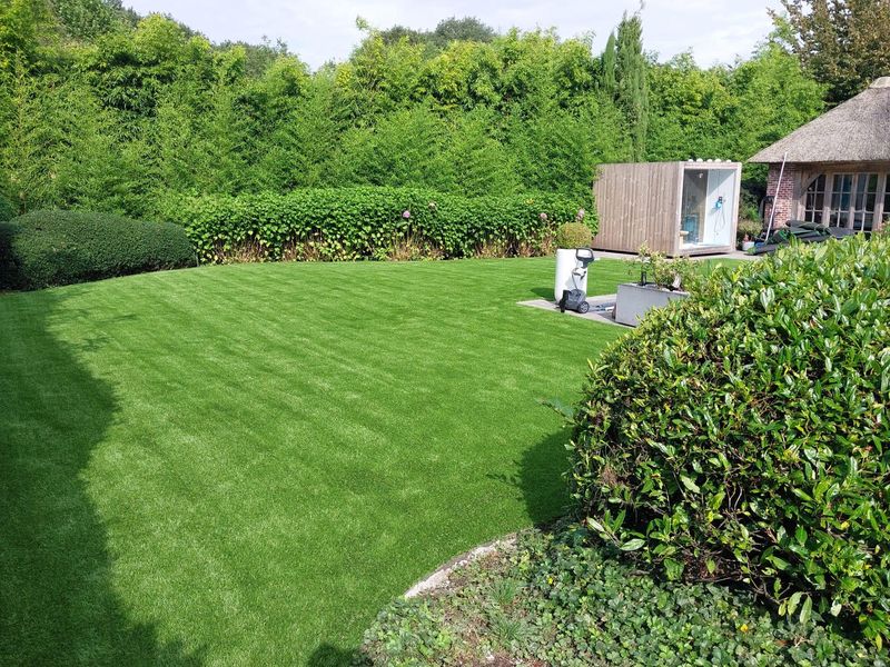 Ruime achtertuin met kunstgras, hagen en een tuinkantoor in Herenthout