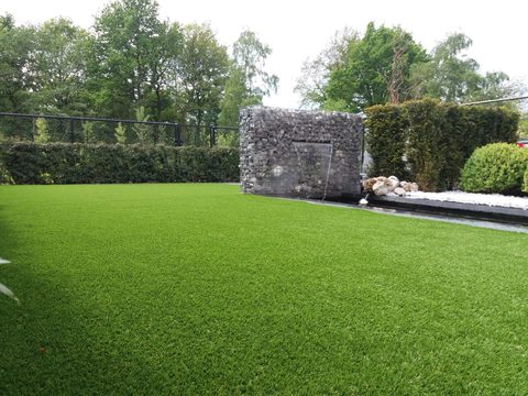 Kunstgras in Berlare, met de gabionwand en buxusbollen op de achtergrond