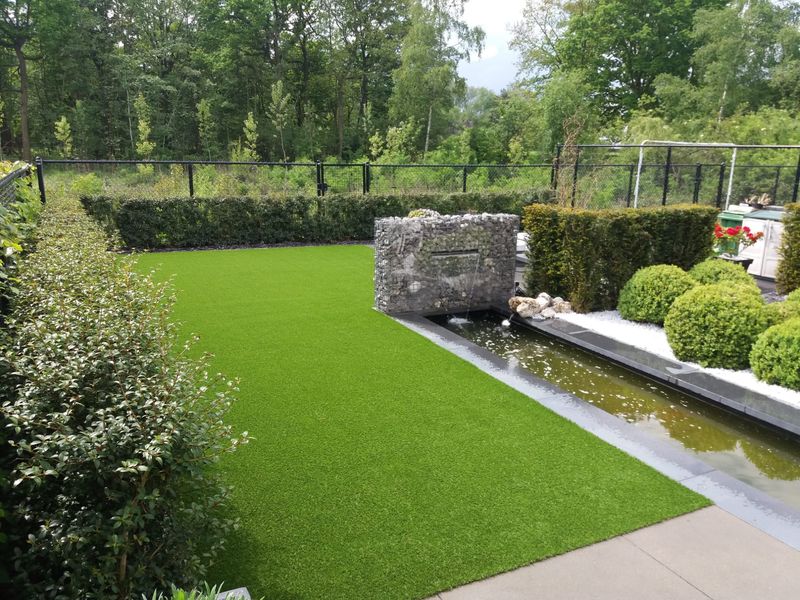 Strakke tuin in Berlare met kunstgras naast een watergoot en een gabionwand met waterval