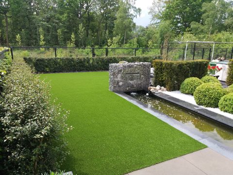 Strakke tuin in Berlare met kunstgras naast een watergoot en een gabionwand met waterval