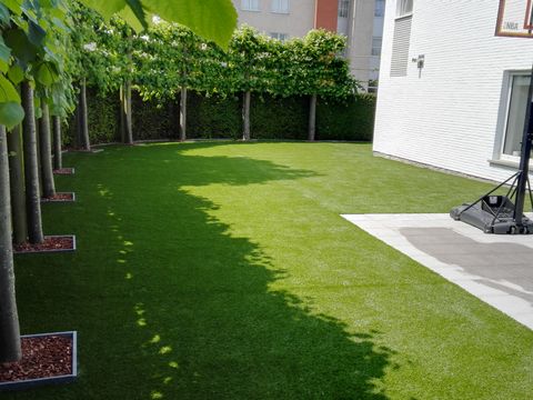 Kunstgras in ForGrass SuperNatural onder een rij leilinden naast een witte gevel in Deinze