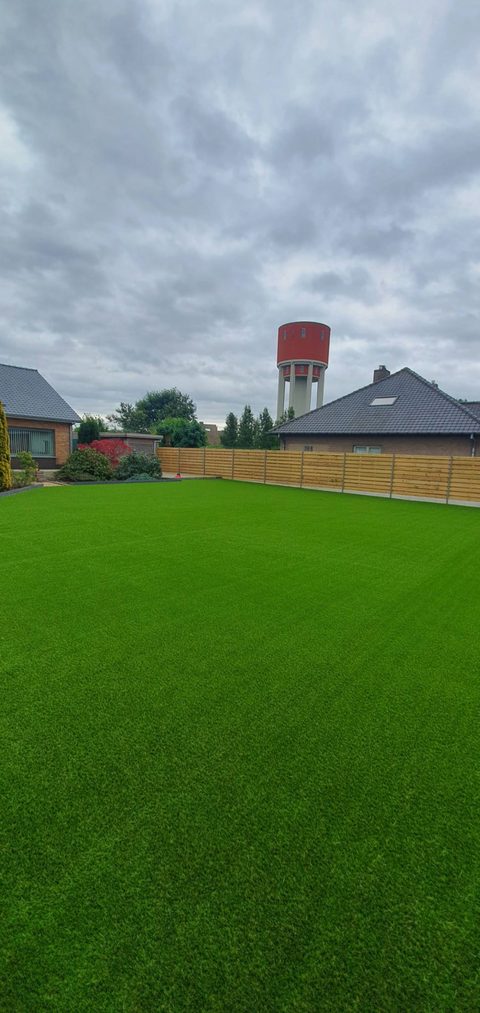 Grote achtertuin in Deinze met kunstgras, met de watertoren op de achtergrond