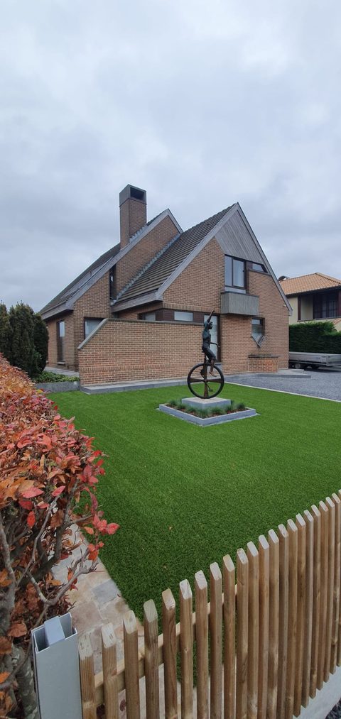 Kunstgras tot tegen de haag en de kastanjehouten afsluiting van een voortuin in Deinze