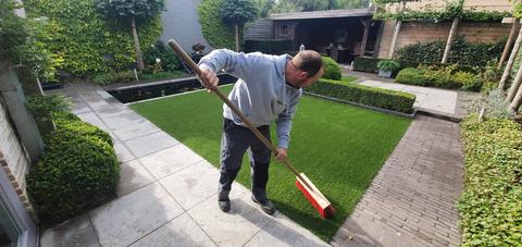 Plaatser borstelt het kunstgras op naast een kleine vijver in een siertuin in Eeklo