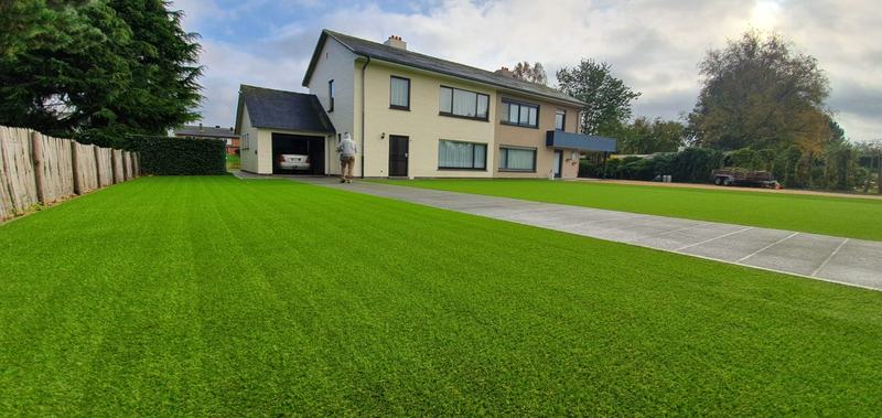 Grote voortuin met kunstgras naast de oprit van een villa in Eeklo, met de plaatser op weg naar de garage