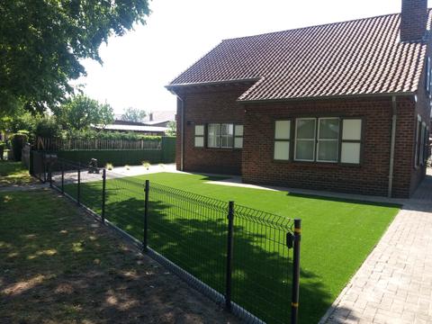 Jardin de façade avec gazon artificiel derrière une clôture grillagée noire, à Evergem