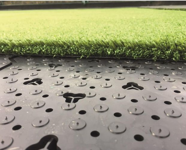 Close-up van een Future Base plaat met perforaties en weerhaken, met het kunstgras erop