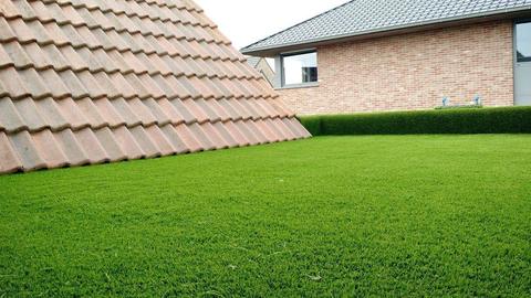 Grande pelouse en gazon artificiel derrière une maison, vue par-dessus le toit en tuiles d&rsquo;une annexe
