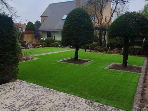 Kunstgras met uitsparingen rond twee bolvormige bomen, naast een kasseioprit