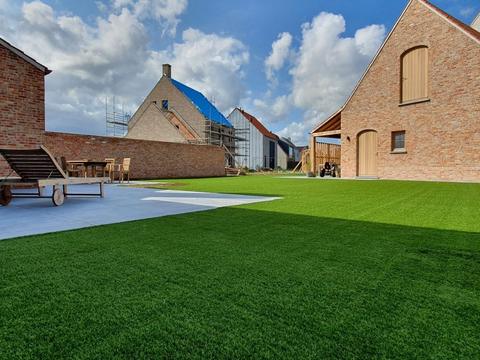 Ruim kunstgrasgazon bij een schuurwoning met terras en ligbedden