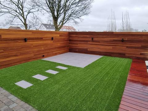 Kleine stadstuin met kunstgras, houten schutting en terras met looptegels