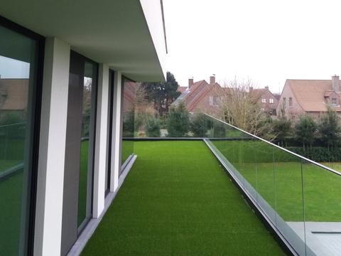Kunstgras op een dakterras langs de raampartij van een villa in Maldegem, met zicht op de buurt