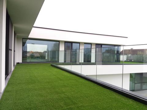 Afgewerkt dakterras met kunstgras langs een glazen balustrade in Maldegem