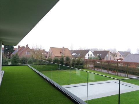 Zicht vanop het dakterras met kunstgras over de tuin en de buurt in Maldegem