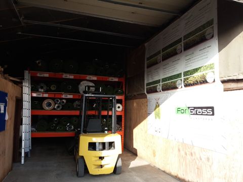 Binnen in de loods in Meigem: rekken met kunstgras, een heftruck en een ForGrass-spandoek met het gamma van toen