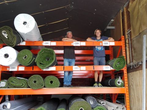 Twee medewerkers van ForGrass tussen de oranje rekken met rollen kunstgras in de loods in Meigem