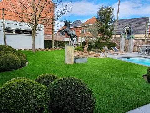 Natuurtuin met kunstgras, snoeivormen en een bronzen beeld in Knesselare
