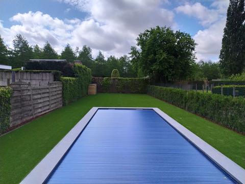 Zwembad met blauw rolluik en kunstgras aan beide zijden tussen hagen in Oudenaarde