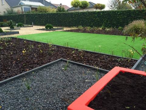 Tuin in Opglabbeek met kunstgras tussen borders van boomschors, grind en een rode plantenbak