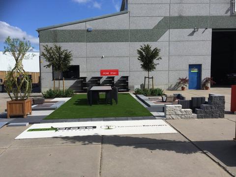 Toonpark met een vlak ForGrass kunstgras, tuinmeubelen en de logo’s van ForGrass en Tuinwerken Reumers in het gras