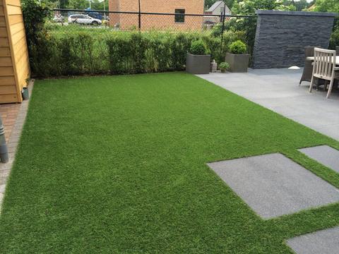 Achtertuin met kunstgras, staptegels en een terras met natuurstenen muur in Limburg