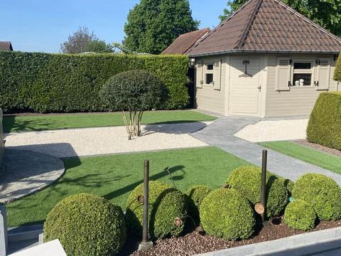 Siertuin met kunstgras, grindpad, buxusbollen en een tuinhuis in Limburg