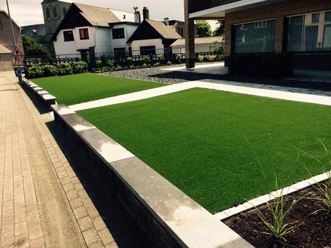 Voortuin met kunstgras in twee terrassen achter een muurtje van natuursteen, aan een kerk in Limburg