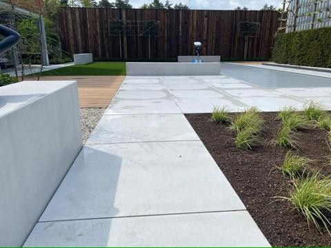 Betonnen terras en zitbanken bij een zwembad met kunstgras op de achtergrond in Limburg