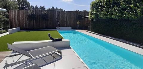 Kunstgras naast een lang zwembad met ligstoelen en een houten wand in Limburg