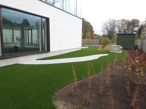 Tuin van een kantoorgebouw in Sint-Denijs-Westrem met kunstgras en een gebogen pad van wit grind langs de glazen gevel
