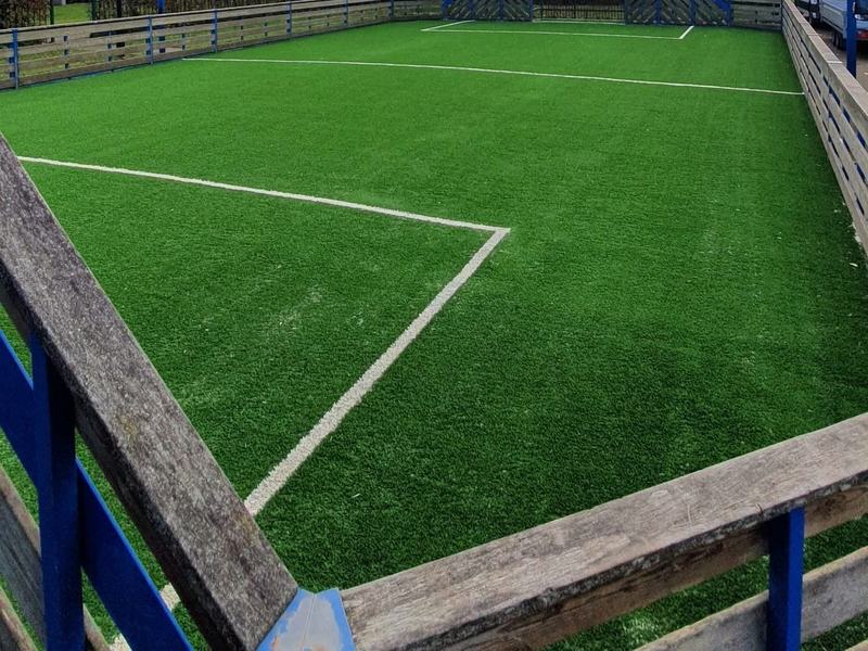 Buurtveld met kunstgras, belijning, doel en basketring tussen appartementsgebouwen