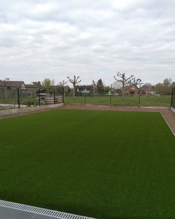 Het kunstgras net gelegd, in het vroege voorjaar met kale bomen