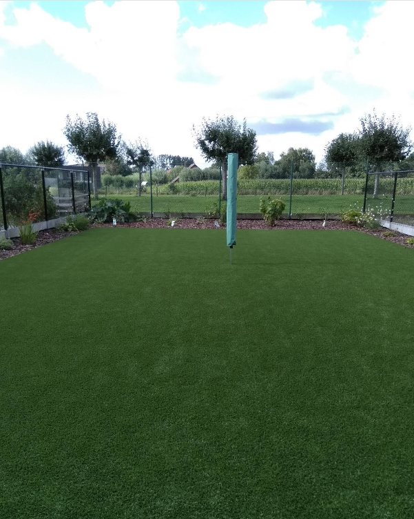 Dezelfde tuin in de zomer, met beplante borders en een droogmolen in het gras