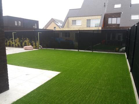 Achtertuin met kunstgras naast een tegelterras, omheind met zwarte schermen, in Stekene