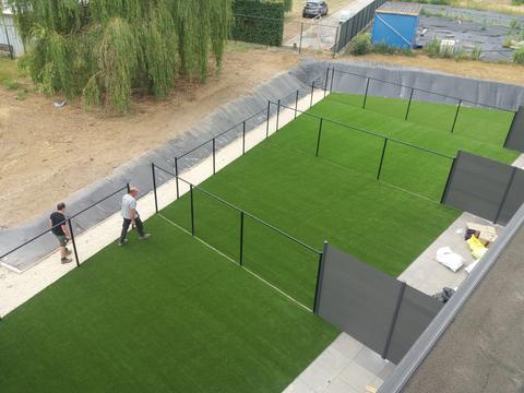 Vier omheinde tuinen in kunstgras naast een appartementsgebouw, gezien van bovenaf, met twee plaatsers van ForGrass