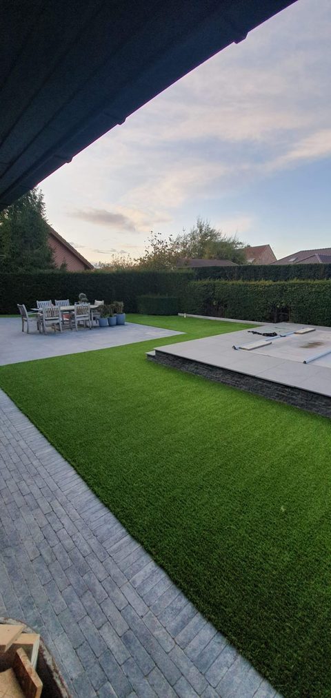 Tuin in Waregem met kunstgras rond een verhoogd terras en een afgedekt zwembad