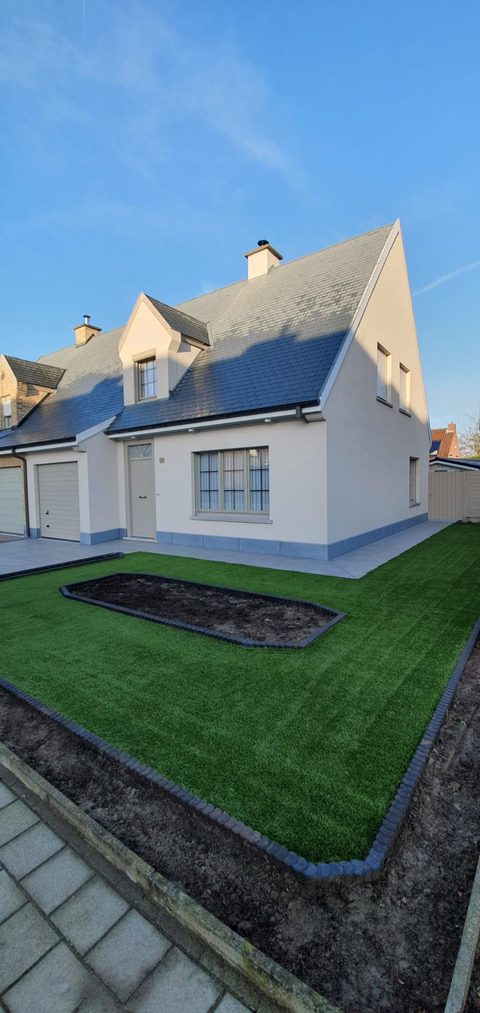 Voortuin van een nieuwbouwwoning in Waregem met kunstgras, boordstenen en een uitgespaard plantvak