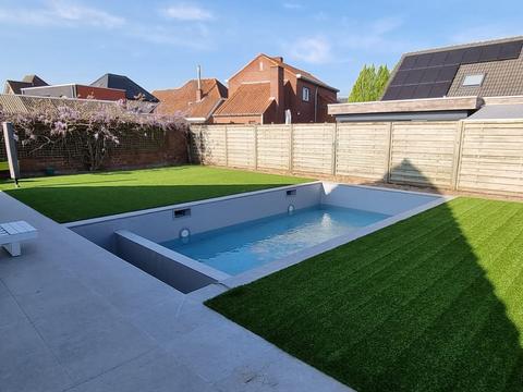 Zwembad met kunstgras eromheen, terras en zitbanken in de Leiestreek