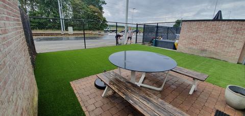 Kleine tuin in Zeebrugge met kunstgras rond een picknicktafel op klinkers, omheind met een draadafsluiting, met de ploeg van ForGrass aan het werk