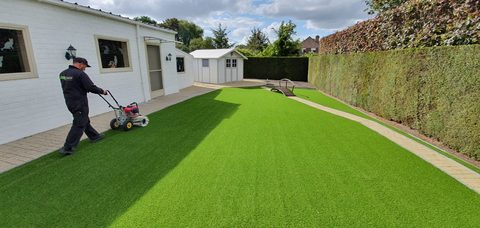 Plaatser van ForGrass borstelt de vezels van pas gelegd kunstgras op in een achtertuin in Zelzate