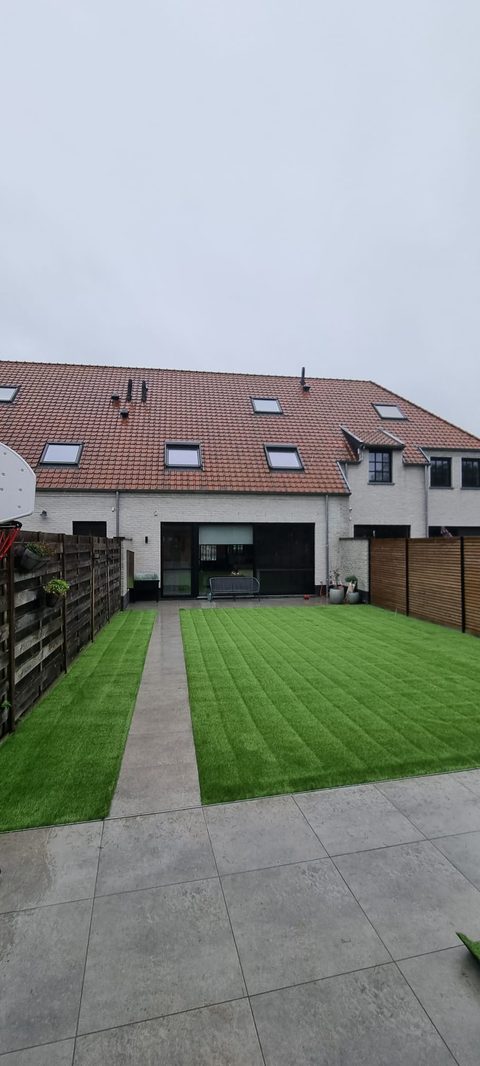 Achtertuin van een rijwoning in Zulte met kunstgras aan weerszijden van een tegelpad